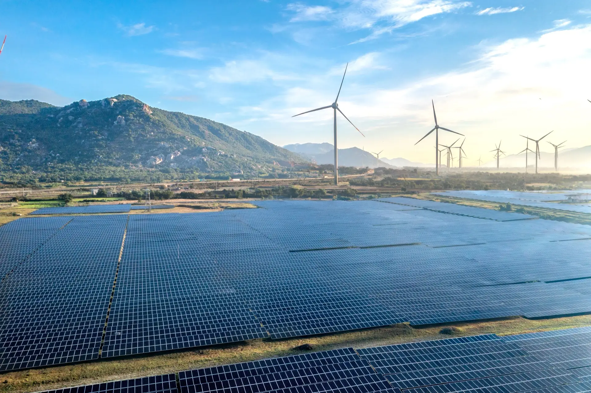 Aerial view of a solar farm with wind turbines beyond